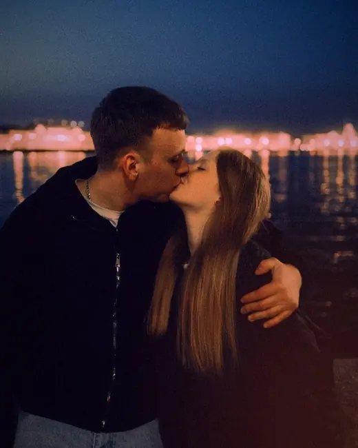 A couple kissing by the water at night, with city lights behind them, with the La La Land look